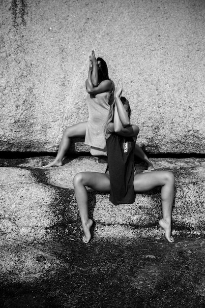 Two beautiful and attractive women practicing yoga outdoors on black and white