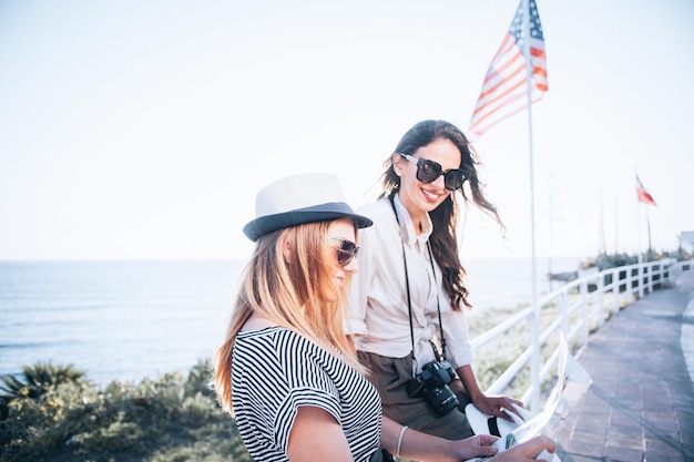 Foto due belle donne bionde e brune con mappa turistica in vacanza. vacanze e concetto di turismo