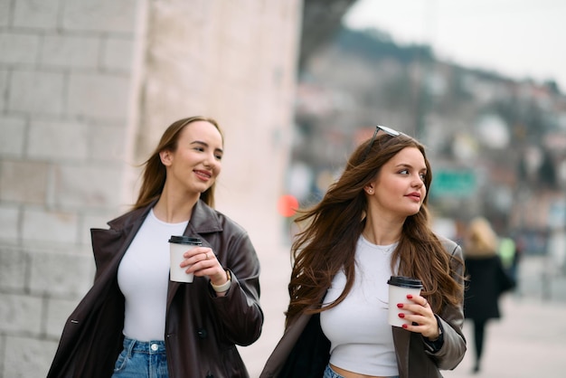 Two beautiful business women go to work while holding cups of coffee in their hands