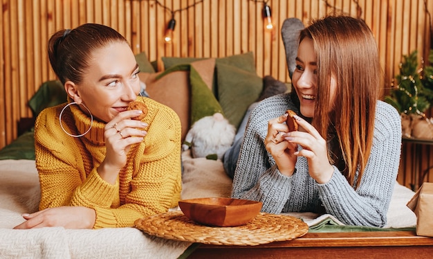 Two beautiful cheerful happy young girls girlfriend give Christmas gifts on the background of a new year tree at home