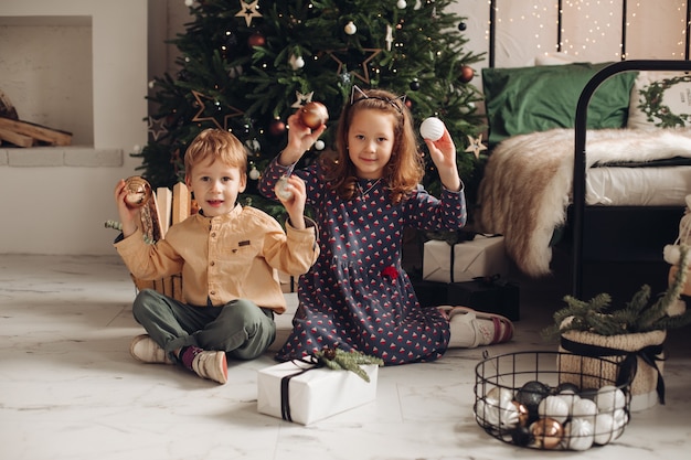 Two beautiful children sit near the Christmas tree