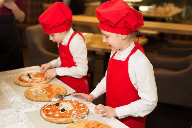 Foto due belle ragazze cuoca in camicie bianche e grembiuli rossi nel ristorante fanno la pizza