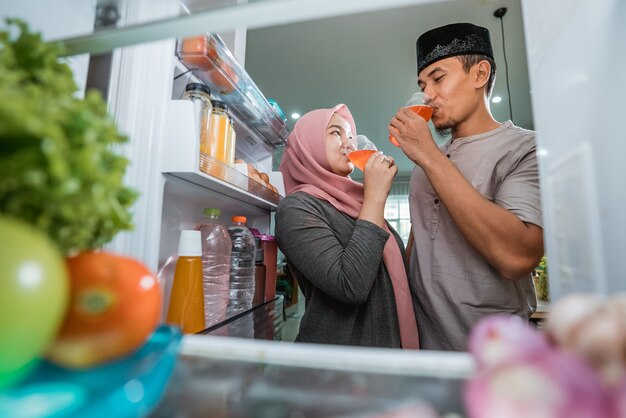 Due belle coppie musulmane che rompono l'iftar veloce davanti al frigorifero aperto in cucina