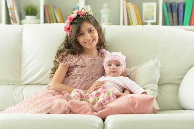 Two beautiful cute sisters posing in sofa at home