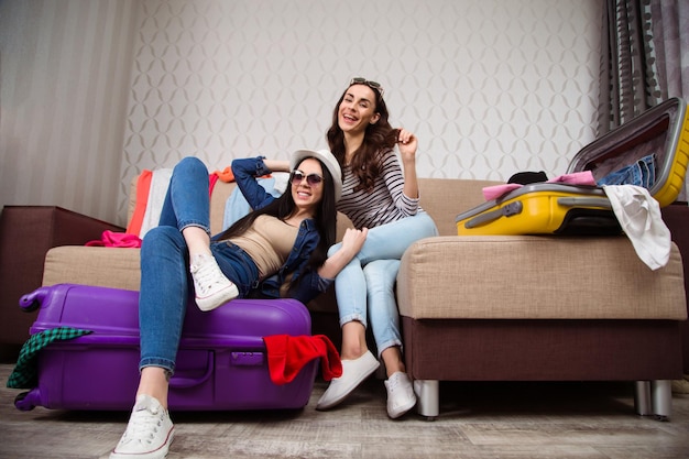 Two beautiful excited cheerful women while folding clothes for a trip to suitcases