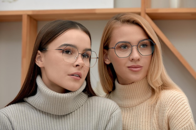 Two beautiful fashion girls in glasses and modern clothes posing with glasses at the camera image of stylish young girls in glasses