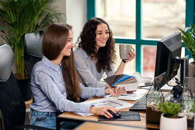 Two beautiful female designers or architects jointly solve work tasks while working in modern office near window. Creative people or advertising business concept.