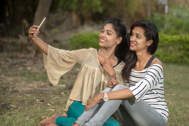 Two beautiful female friends taking selfie with smartphone in outdoors.