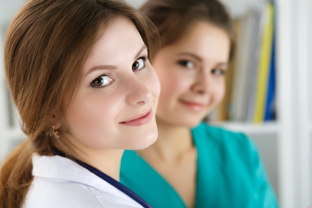 Two beautiful female medicine doctors working at their office discussing diagnose and filling patient registration or medical history form