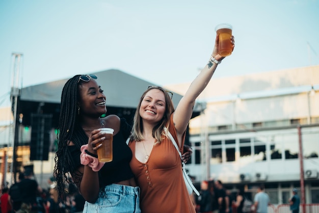 Two beautiful friends drinking beer and having fun at music festival