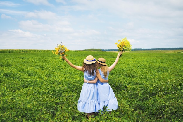 Due belle amiche in cappelli che abbracciano nel campo verde