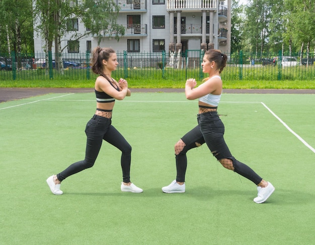 Two beautiful girls doing exercises lunges on the Playground.