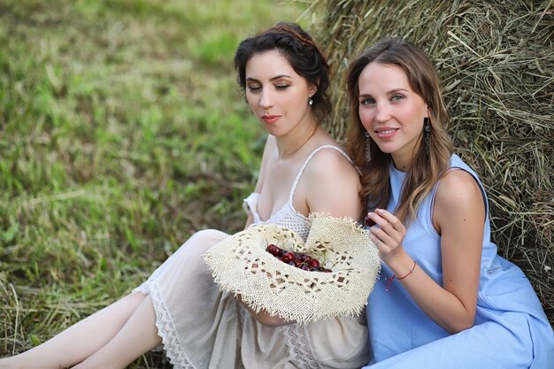 Two beautiful girls in dresses in summer field with berries