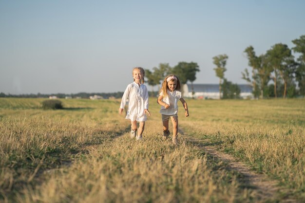 두 명의 아름다운 소녀가 마을의 어린 시절 잔디 사이에서 행복하게 들판으로 뛰어듭니다.