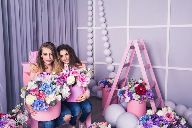 Two beautiful girls in jeans and pink sweater with decor of flowers in baskets