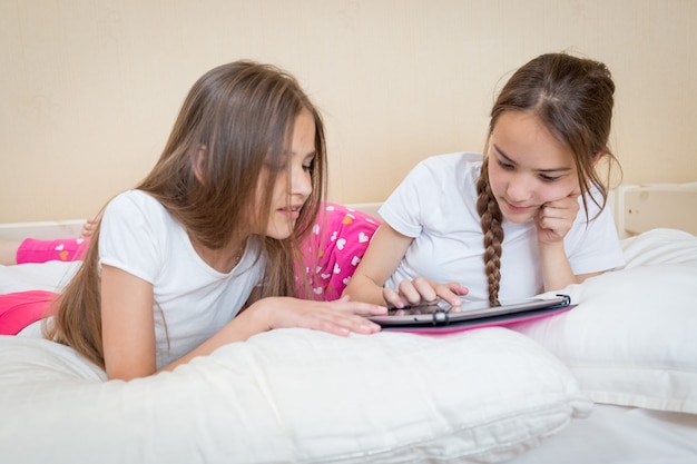 Two beautiful girls in pajamas lying and using digital tablet