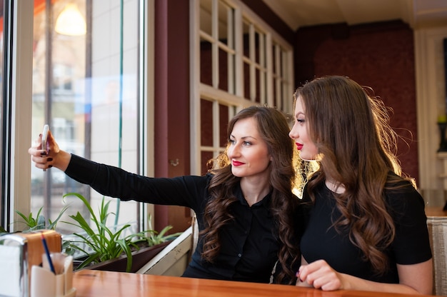 Two beautiful girls do selfi and drink coffee