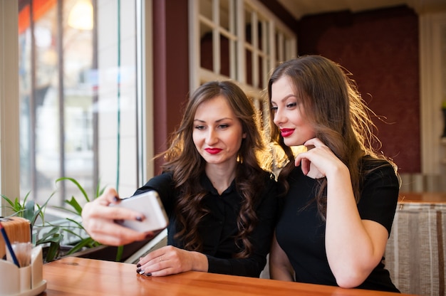 Two beautiful girls do selfie and drink coffee