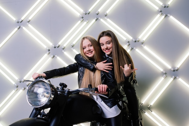 Two beautiful girls wearing costumes of racers and sitting on a motorcycle, in the studio