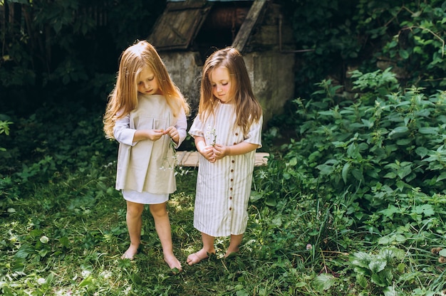 Two beautiful girls in white antique shirts near a well on a background of grass and trees