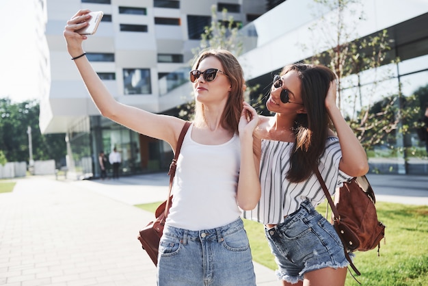 Красивая молодая счастливая девушка студента 2 с рюкзаком около кампуса университета и делает фото selfie. Концепция образования и досуга