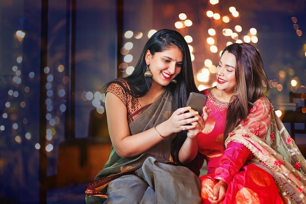 Two beautiful Indian women in ethnic clothes doing Diwali shopping online using mobile phone