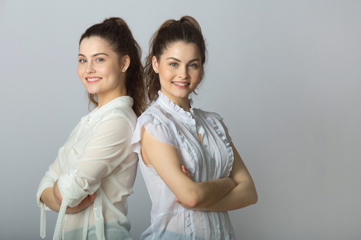 Photo two beautiful joyful women twins on a gray background
