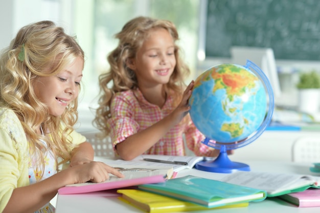 Two beautiful little girls at class reading book and  looking at globe