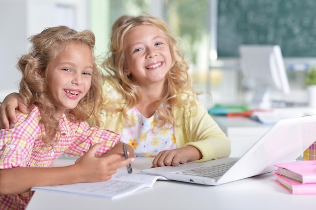 Two beautiful little girls at class using laptop and writing