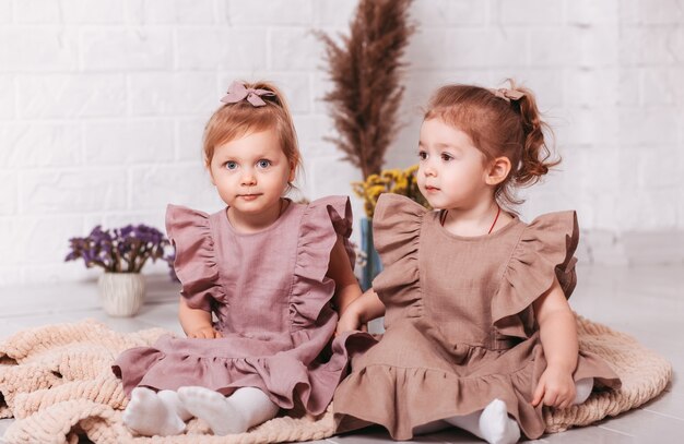 Photo two beautiful little girls in identical dresses sit next to each other