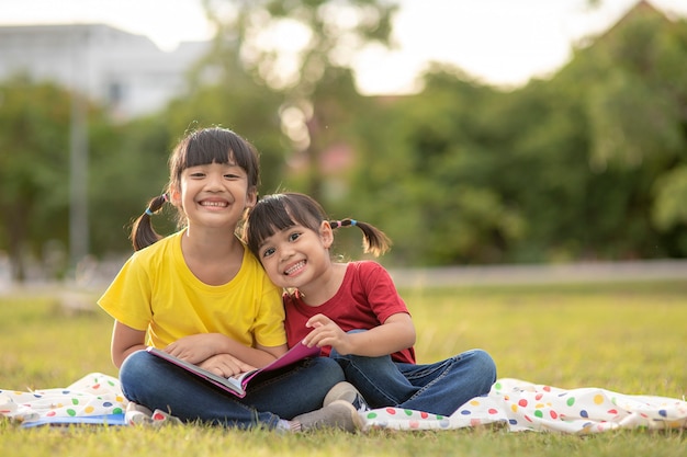 잔디에 앉아 정원에서 책을 읽고 두 아름 다운 작은 소녀. 교육과 우정의 개념입니다.