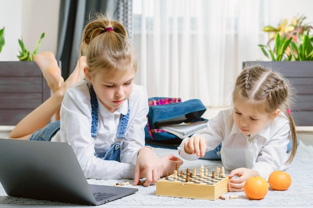 Two beautiful little sisters playing chess on a floor in living room