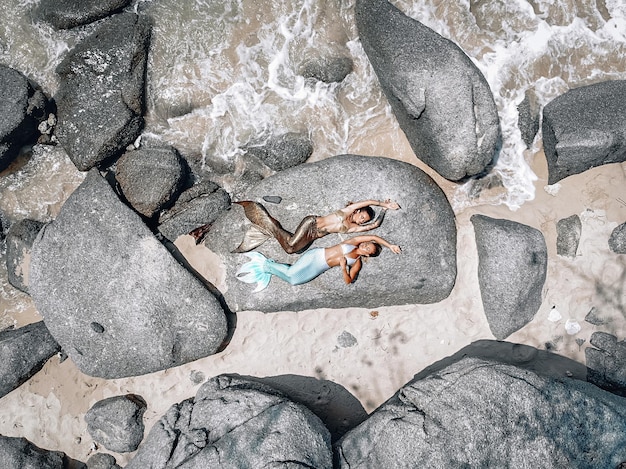 two beautiful mermaids are lying on the stones and sunbathing near the ocean, relaxing, top view