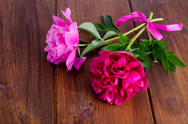 Two beautiful peonies with ribbon on wooden table