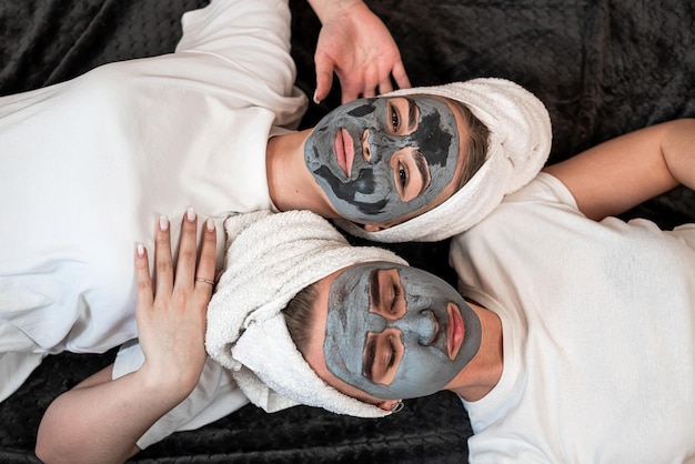 Photo two beautiful sister lying on the floor with clay mask on face