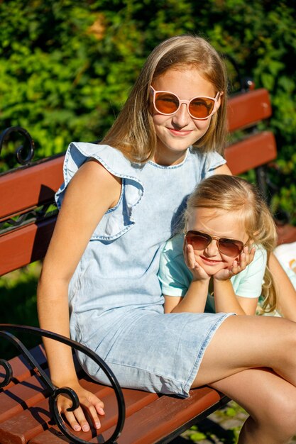 Two beautiful sisters in blue dresses are sitting in the park