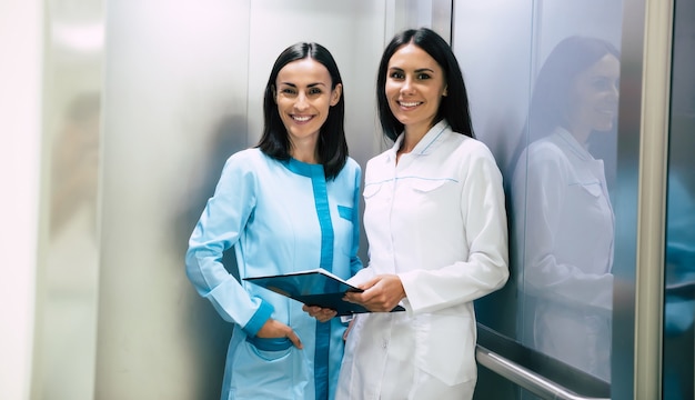 Two beautiful smiling confident women doctors in the elevator have a conversation about some patient