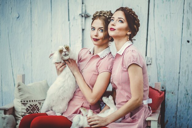 two beautiful twin sisters sit with rabbits