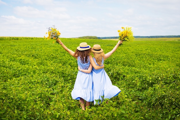 Two beautiful womanfriends in hats hugging in green field