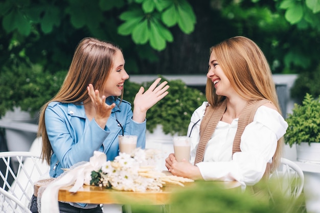 Due belle donne sono sedute a un tavolo in una caffetteria e comunicano emotivamente, sorridendosi a vicenda