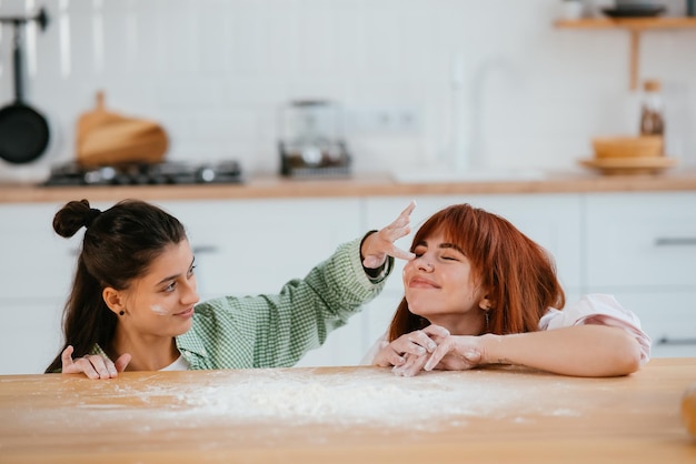 Две красивые женщины играют с мукой на кухне