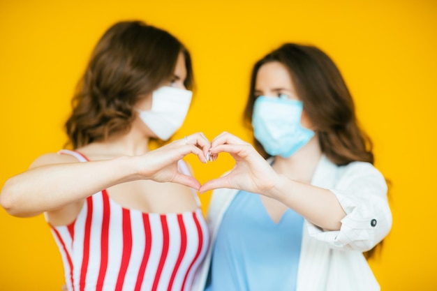 two beautiful women in protective masks on yellow background pandemic coronavirus virus protection