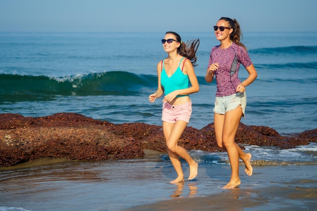 Two beautiful women run along the beach in the summer morning.cardio workout healthy lifestyle sport .girlfriends doing sports on the ocean waves and sea breeze tropics,SPF protection