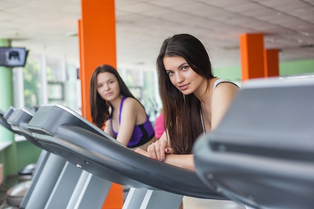 Two beautiful women running on the treadmill in the gym. Pretty girls on the running track indoors training and smiling