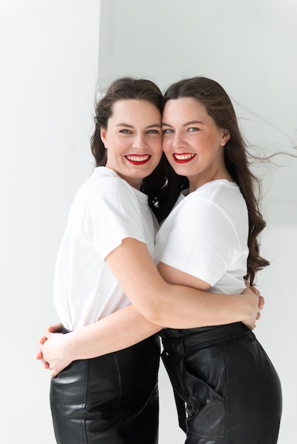 Two beautiful women twin sisters posing white background