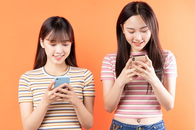 Two beautiful young asian girls are using mobile phones on orange wall