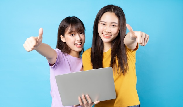 Two beautiful young asian girls using laptop on blue wall