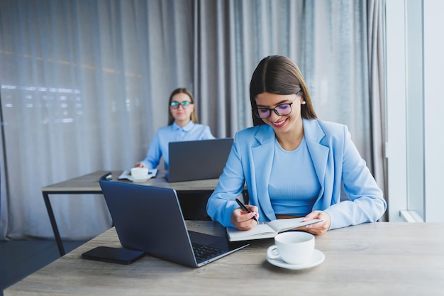 Two beautiful young business women are working and discussing work points in the office Girlfriends at workplaces in the office Large modern office with windows