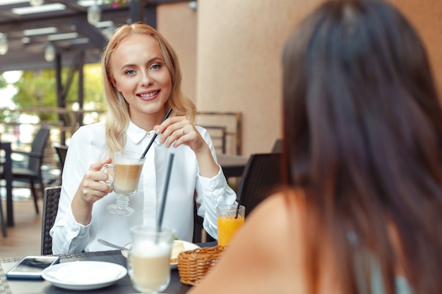 Two beautiful young girls sitting by the table in cafe