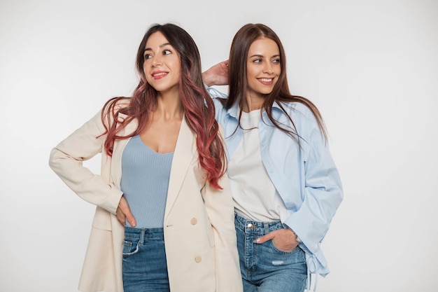 Foto due belle giovani amiche felici donne in abiti casual denim alla moda con una giacca camicia e jeans in posa e divertirsi in studio su sfondo bianco